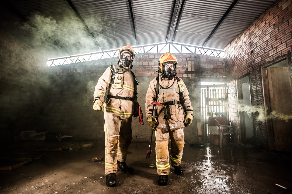 Two firefighters in protective equipment in an old factory building.