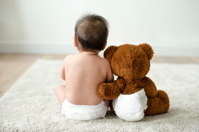 Back of a baby and a stuffed teddy bear in nappies