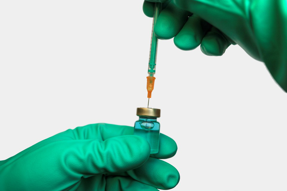 Person wearing medical gloves draws a vaccine from an ampoule with a syringe.