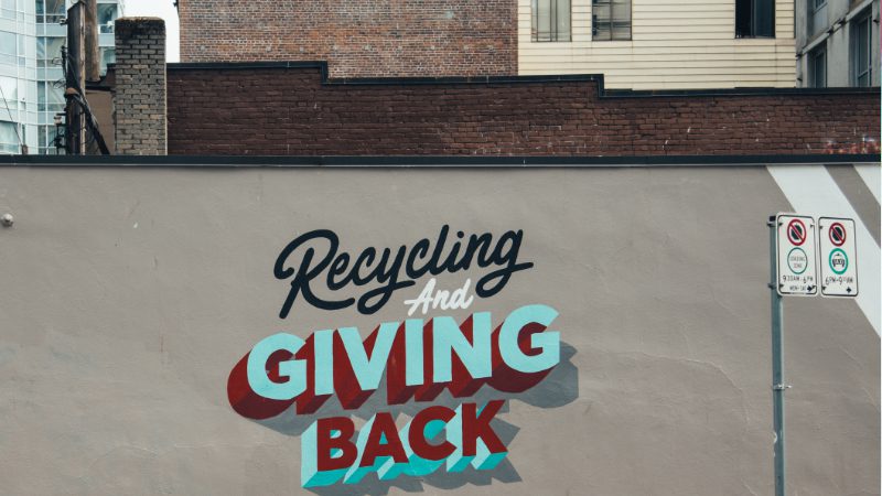 Gray wall in a city with the slogan "Recycling and giving back" .