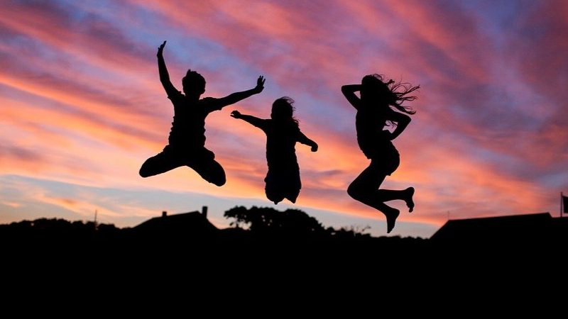 3 healthy people jump in the background of a sunset demonstrating their fitness.