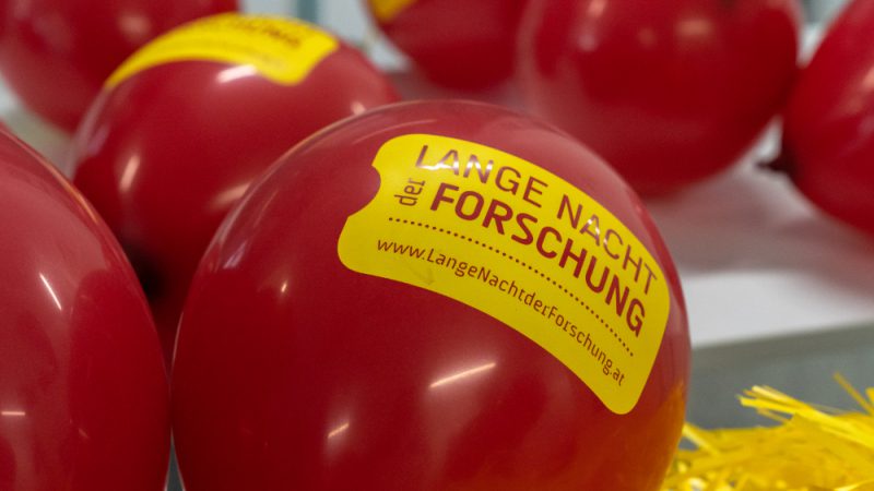 The picture shows red balloons printed with the logo "The long night of research".