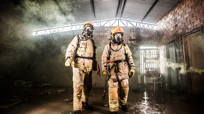 Two firefighters in protective equipment in an old factory building.