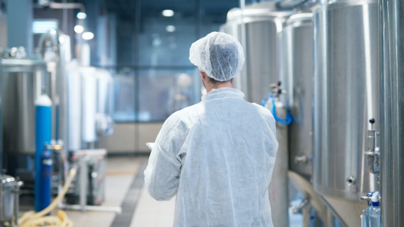 Technologist in white protective suit walking through food factory production line checking quality