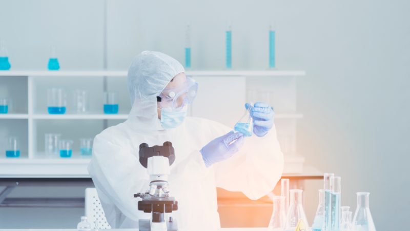 Scientist in laboratory looks at test tube with blue liquid