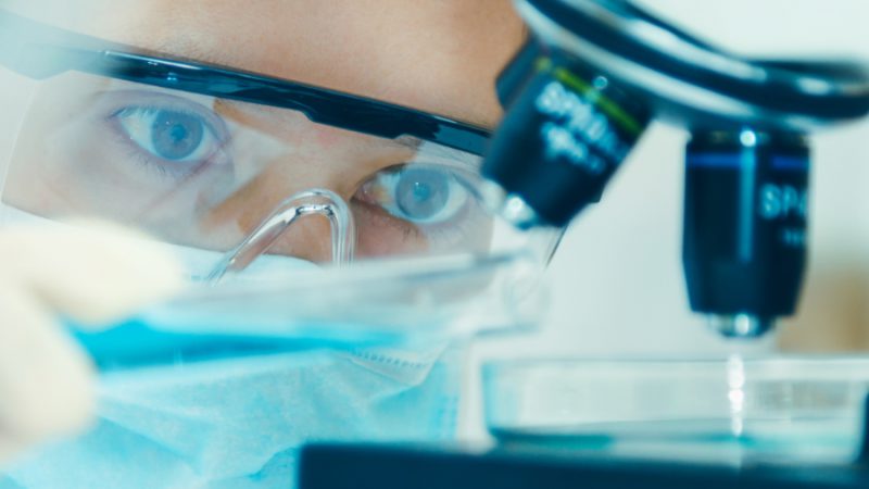 Scientist in goggles looking at a microscope