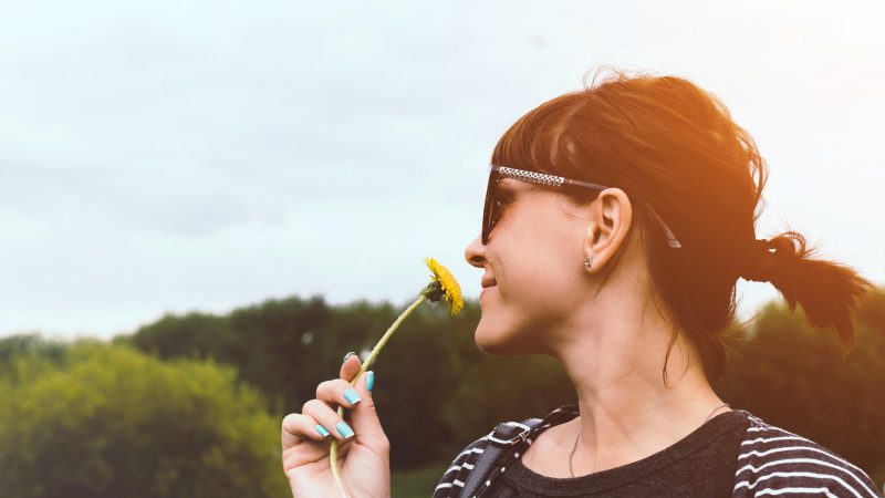 Brunette woman smelling a dandelion.