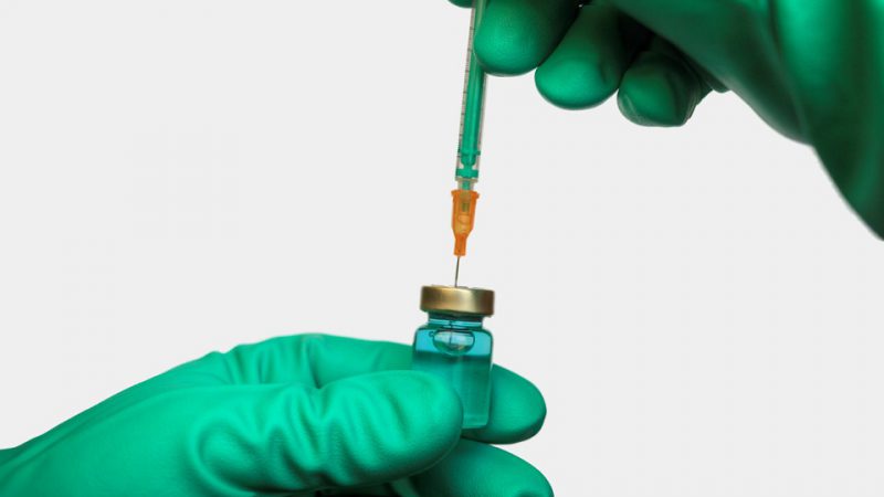 Person wearing medical gloves draws a vaccine from an ampoule with a syringe.