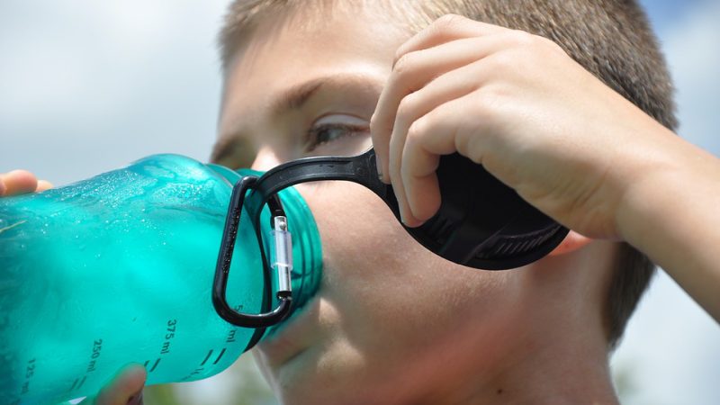 Little boy enjoying water from blue transparent water bottle.