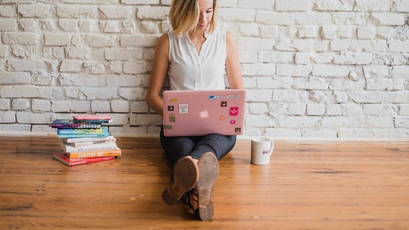 Young woman sitting on the floor writing something on her laptop